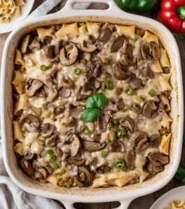 Philly cheesesteak casserole with sliced mushrooms, tender steak, pasta, and creamy cheese sauce garnished with fresh basil in a white baking dish.