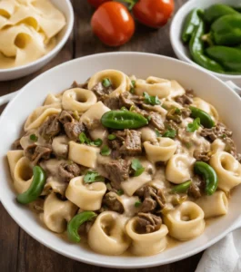 Cheesesteak tortellini in a creamy provolone sauce garnished with fresh herbs and peppers.