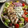 Greek chicken salad with grilled chicken, tzatziki sauce, feta, olives, and tomatoes in a bowl