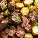 Juicy garlic butter steak bites with crispy roasted potatoes garnished with fresh parsley, served in a dark bowl.