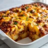 A close-up of a freshly baked hamburger potato casserole in a white baking dish, with a serving removed to show the layers of seasoned ground beef, sliced potatoes, and melted cheddar cheese.