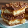 A close-up of stacked cake mix toffee bars on a blue plate, showing the layers of golden crust, cheesecake filling, caramel, chocolate, and a crunchy toffee nut topping.