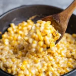 Close-up of creamy honey butter skillet corn being scooped with a wooden spoon.