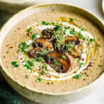 Close-up of a bowl of creamy keto diet cream of mushroom soup, garnished with sautéed mushrooms, fresh herbs, and a drizzle of olive oil.
