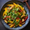 Mango chicken stir fry with bell peppers and cilantro in a black bowl