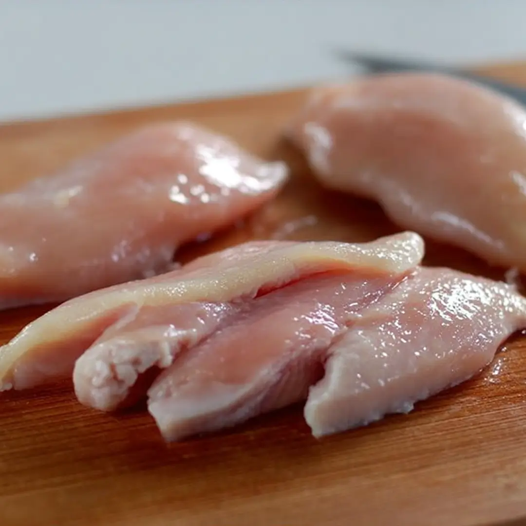 Raw chicken breasts sliced on a wooden cutting board