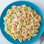 Imitation crab pasta salad with creamy dressing, green peas, and shell pasta served on a blue plate