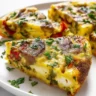 Slice of golden-brown keto frittata recipe with visible vegetables like red bell pepper and zucchini, garnished with fresh parsley on a white plate.
