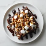 Close-up of a Mississippi mud cake mix slice topped with marshmallows, chopped walnuts, and chocolate drizzle on a white plate