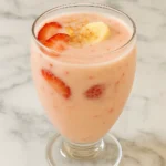 Strawberry banana protein shake in a glass with fresh strawberry slices and banana pieces