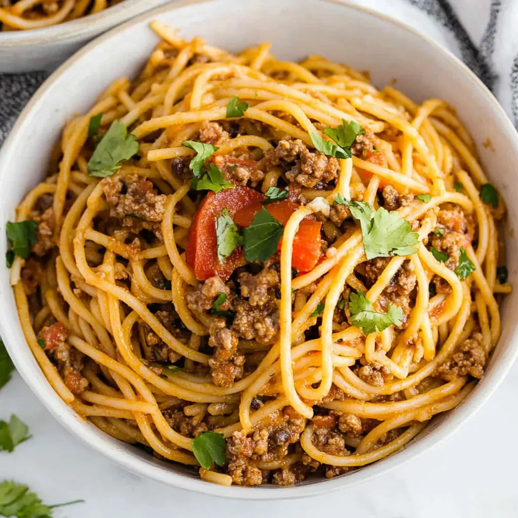 Taco spaghetti recipe easy with ground beef, spaghetti noodles, and fresh cilantro in a bowl