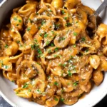 Close-up of a bowl of creamy one pot French onion pasta with caramelized onions, sliced mushrooms, and a sprinkle of fresh parsley and grated cheese, ready to eat.