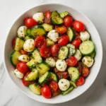 Bowl of cucumber tomato and mozzarella salad with fresh basil and dressing