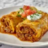 A close-up of two golden-fried chimichangas on a white plate, showcasing the delicious final dish from this beef and cheese chimichanga recipe