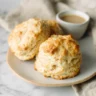 Three golden-brown homemade biscuits on a rustic plate, showcasing the results of an easy biscuit recipe with no buttermilk