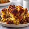 A close-up image of a serving of savory cornbread and sausage stuffing on a white plate, highlighting its moist, crumbly texture and crispy, golden-brown top.