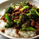 A close-up of a white bowl filled with fluffy rice and topped with a savory ground beef and broccoli stir-fry in a glossy sauce.
