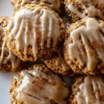 A close-up of chewy vanilla pumpkin oatmeal latte cookies, piled on a plate, with a creamy vanilla glaze and a sprinkle of cinnamon.