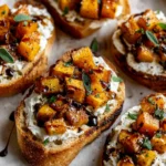 Golden bruschetta topped with caramelized butternut squash and apples, drizzled with balsamic reduction and fresh herbs.
