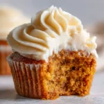 Soft pumpkin cupcake with creamy cinnamon cream cheese frosting, partially eaten to show moist texture