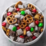 Holiday muddy buddies with pretzels, red and green M&Ms, and chocolate Chex mix in a festive snack mix bowl.