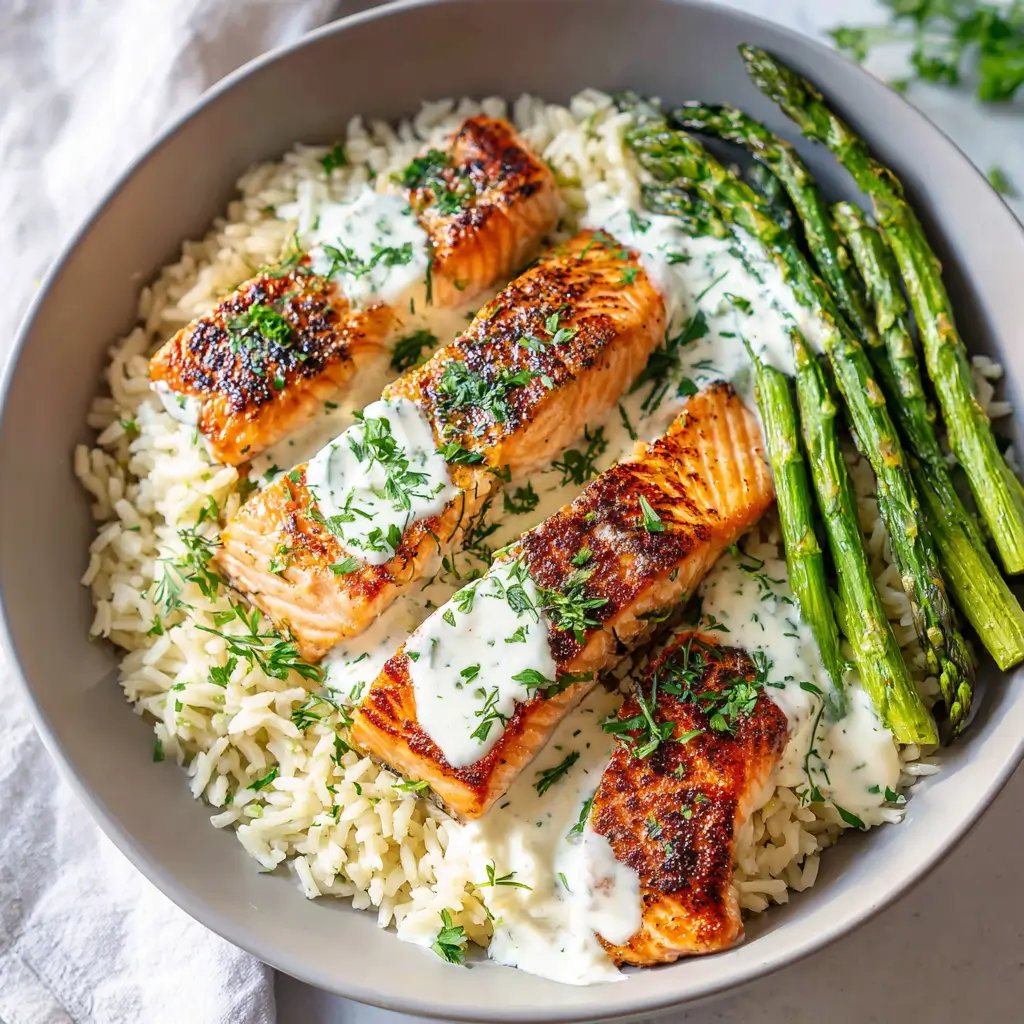 Seared salmon over rice, drizzled with creamy herb sauce and served with roasted asparagus