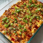 Spicy salmon sushi bake casserole topped with sriracha drizzle, scallions, and nori in a glass dish