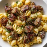 Juicy garlic butter steak bites atop creamy Parmesan shell pasta, garnished with fresh herbs.