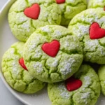 Bright green crinkle cookies with red heart candies and powdered sugar.