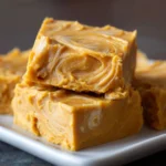Pieces of creamy banana fudge with a light golden color and subtle swirls, stacked on a white plate.