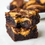 Close-up of two rich, fudgy brownies stacked, filled with a gooey swirl of golden Biscoff cookie butter and topped with crisp bits of Biscoff cookie.