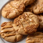 Close-up of chewy, golden Biscoff cookies drizzled with glossy Biscoff cookie butter, highlighting their crispy edges and crackly tops.