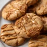 Close-up of chewy, golden Biscoff cookies drizzled with glossy Biscoff cookie butter, highlighting their crispy edges and crackly tops.