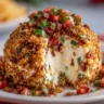 A cut-open bruschetta cheese ball coated in crispy breadcrumbs, filled with creamy cheese and fresh herbs, and topped with a vibrant tomato bruschetta mixture.