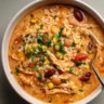 A comforting bowl of chipotle chicken soup filled with shredded chicken, rice, corn, kidney beans, pinto beans, tomatoes, and a creamy, smoky broth, finished with a sprinkle of fresh parsley and served with a spoon.