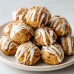 Protein bites drizzled with white icing, stacked on a plate, with a cinnamon-sugar dusting.​