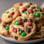 A plate of classic Christmas cookies loaded with red and green M&M’s and chocolate chips, stacked in a festive pile. The cookies are golden, soft, thick, and studded with colorful chocolate candies.
