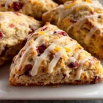 Orange Cranberry Scones on a plate, golden-brown and studded with cranberries, drizzled generously with sweet orange glaze.