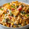 A vibrant bowl of creamy chili cheese Fritos salad, layered with crunchy corn chips, black beans, corn, red and green bell peppers, scallions, and a rich cheese dressing.