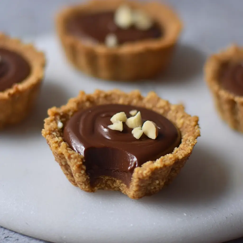 Mini nutella tartlets with chocolate hazelnut filling, flaky nutty crust, white chocolate pieces, and bite taken from one.