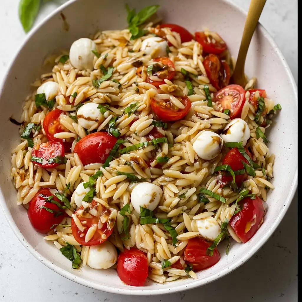 Cold orzo caprese pasta salad with basil, balsamic glaze, mozzarella balls, and tomatoes in bowl
