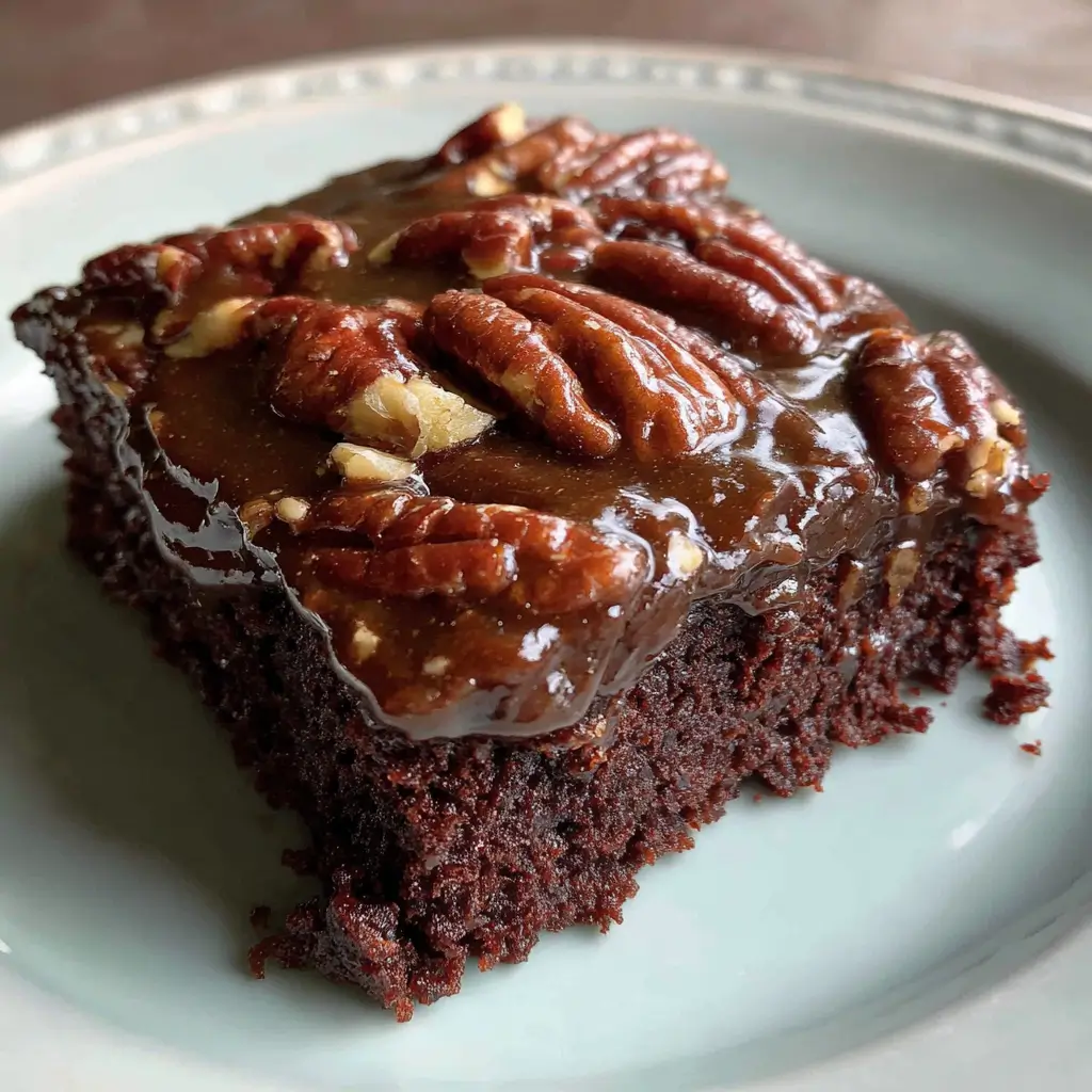 rich, chocolate brownie topped with pecans and a glossy caramel glaze, served on a light-colored plate.
