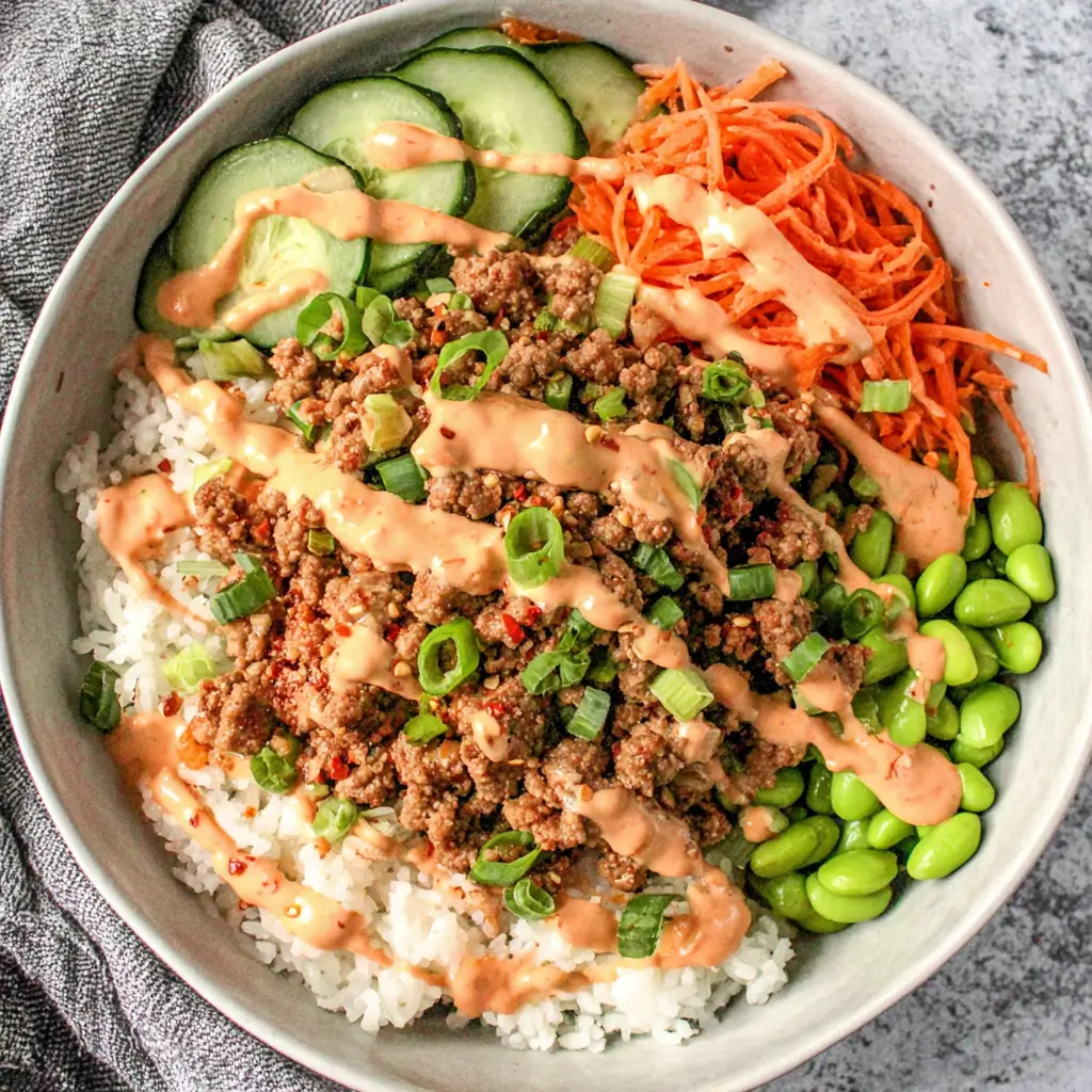 Bang Bang ground turkey bowls with white rice, seasoned ground turkey, edamame, shredded carrots, cucumber slices, and creamy bang bang sauce.