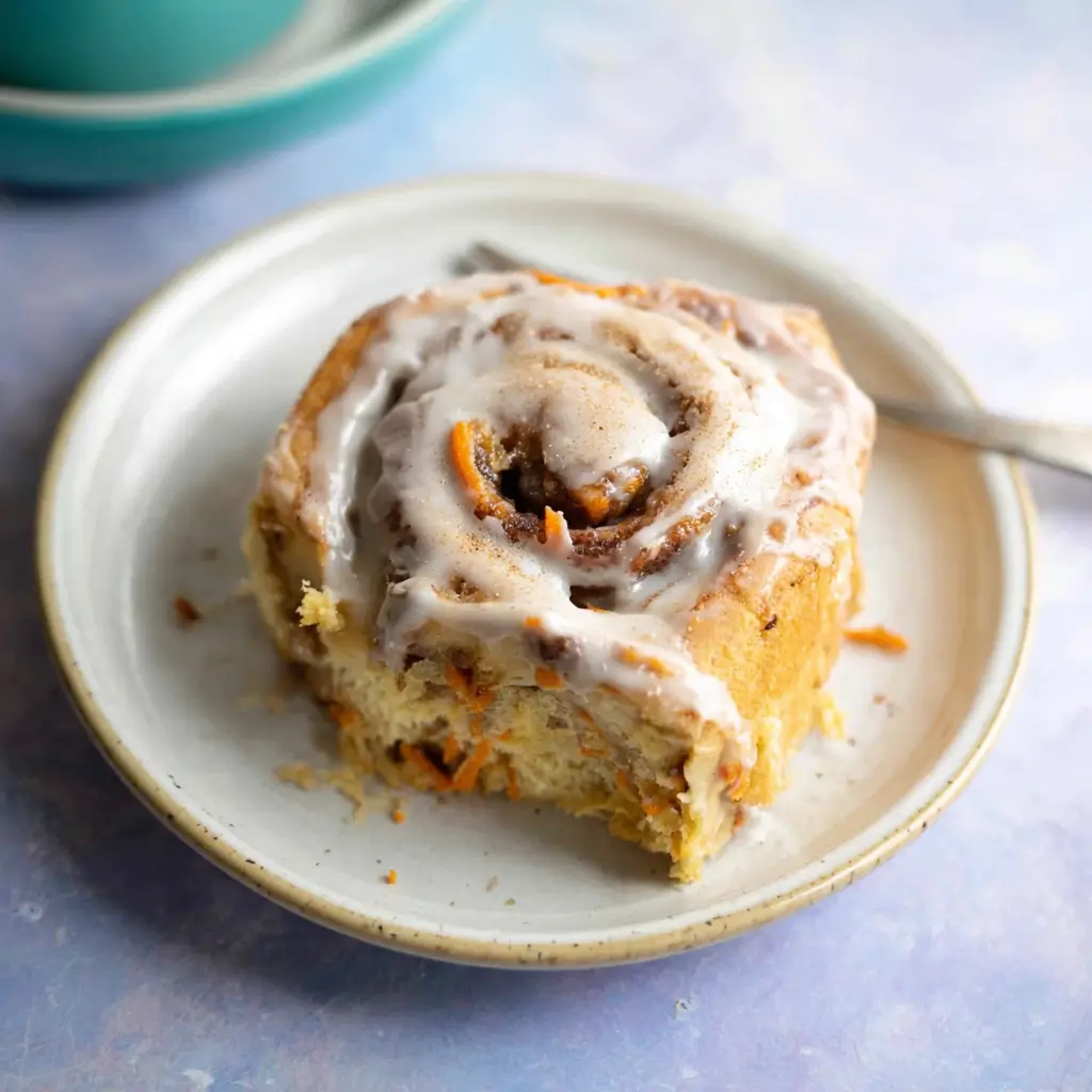 A cinnamon roll topped with a generous drizzle of glaze, served on a small white plate with a fork beside it.