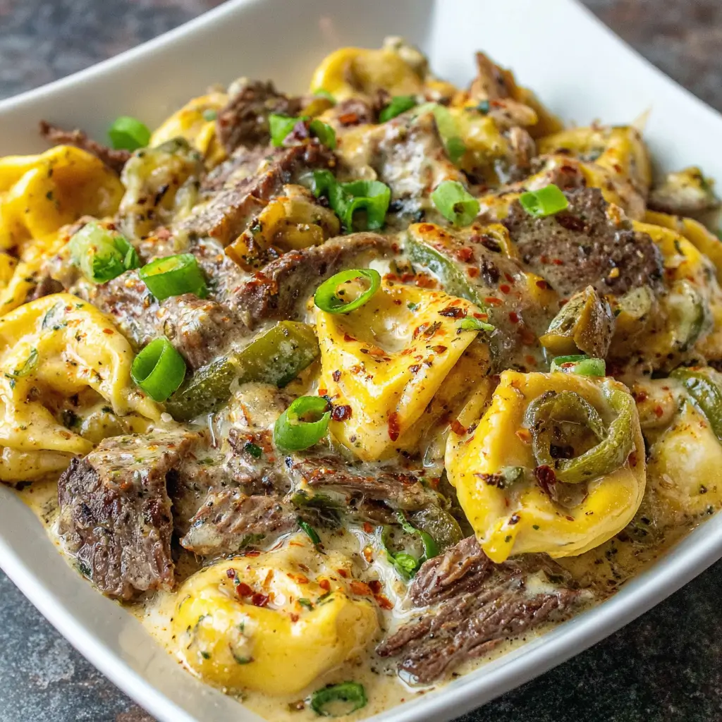 A close-up of a bowl of cheesy beef and tortellini soup garnished with chopped green onions, featuring tender beef, tortellini pasta, and a creamy, seasoned broth.