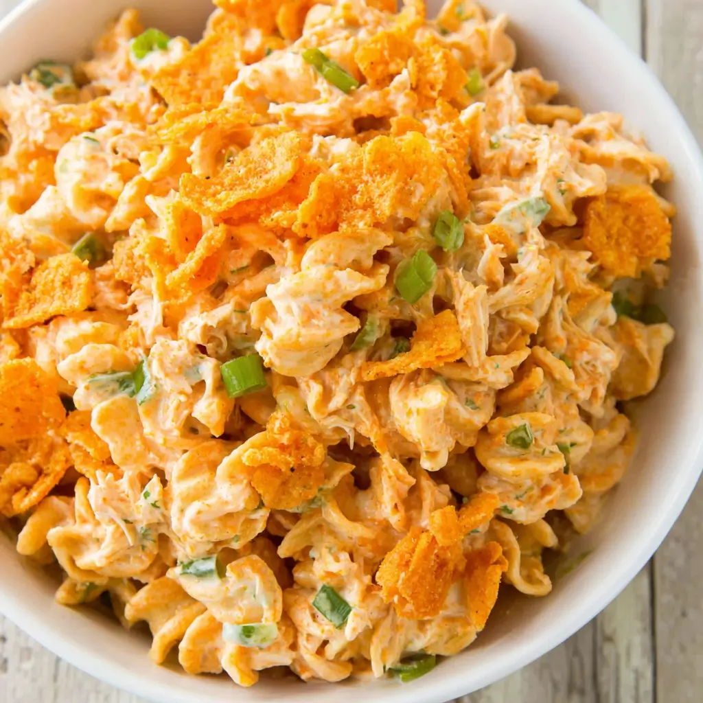 Doritos chicken pasta salad with rotini pasta, shredded chicken, creamy orange dressing, green onions, and crushed Doritos on top.