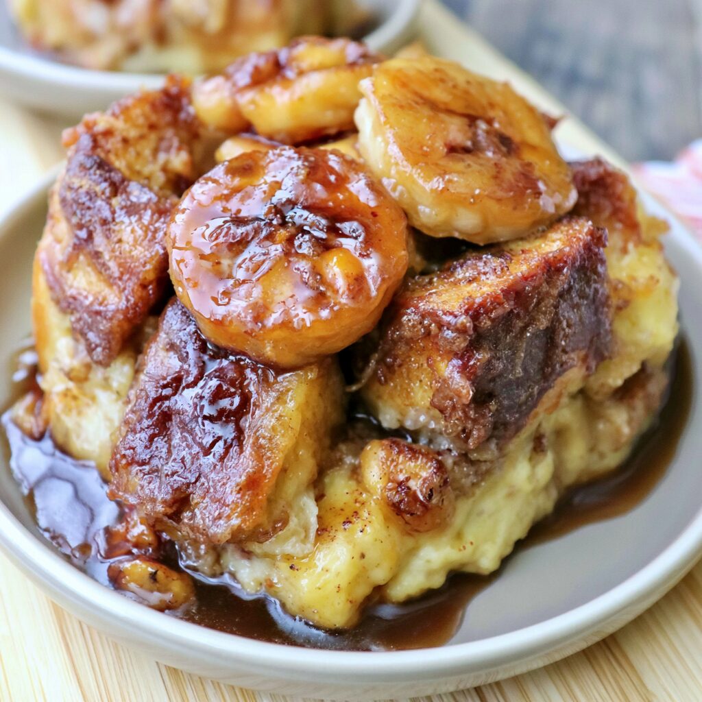 An individual serving of warm bread pudding topped with thick, caramelized banana rounds and a luscious dark syrup.