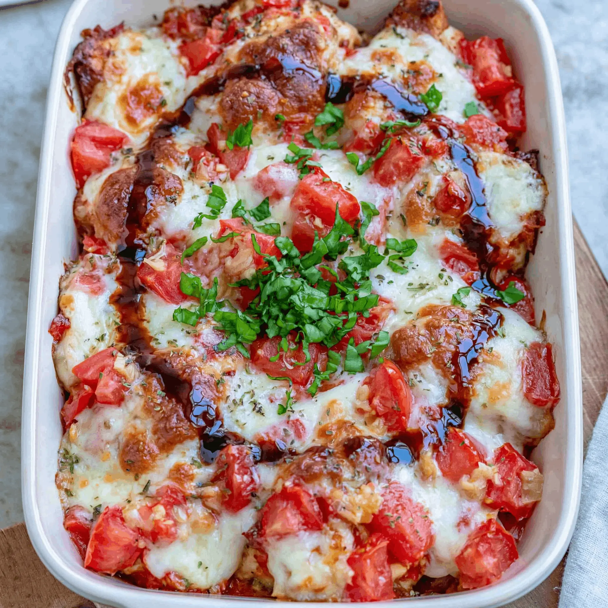 Baked cheesy chicken and tomato casserole topped with herbs and drizzled with balsamic glaze.