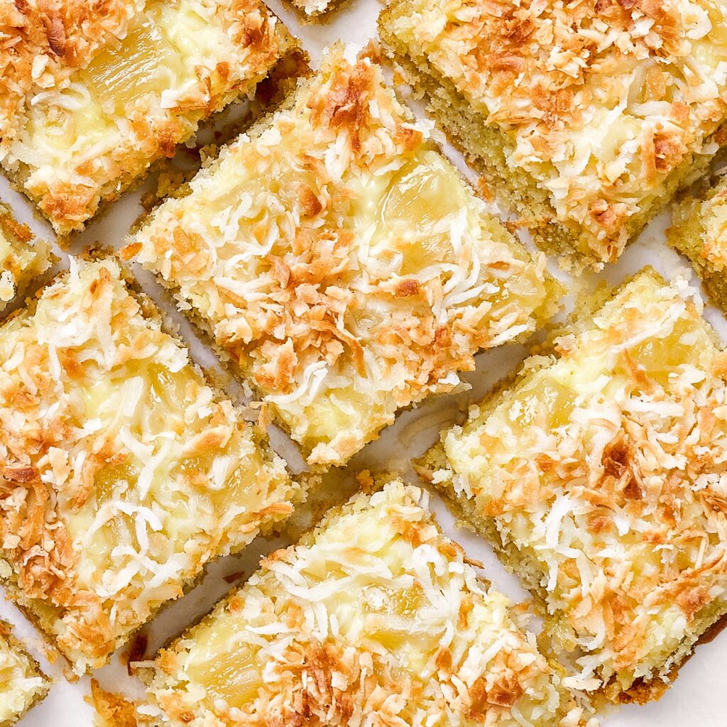 An overhead view of several square pineapple coconut cookie bars with visible pineapple chunks and a golden-brown toasted coconut topping.
